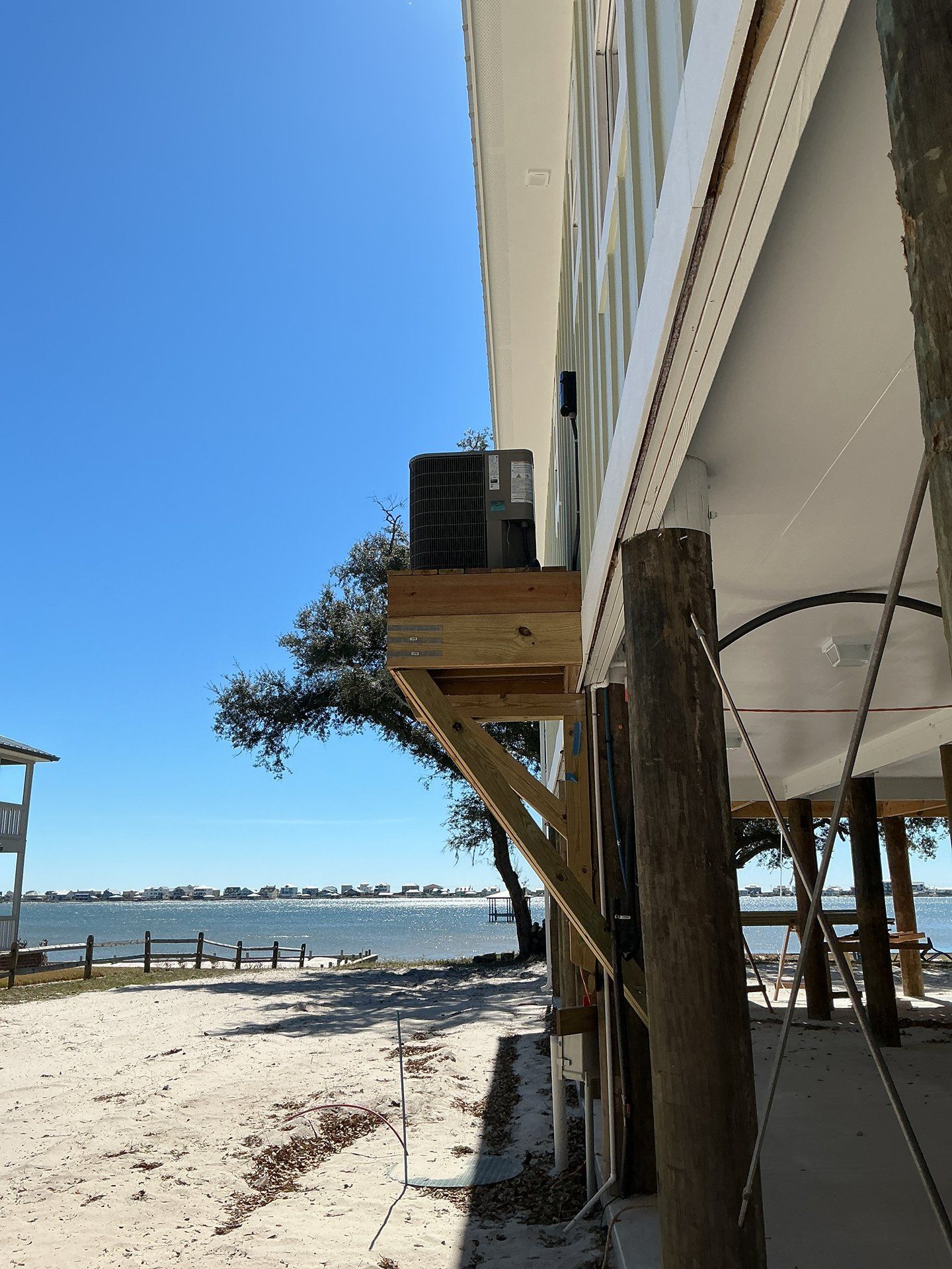 Beachside building with a wooden deck and air-conditioning unit, overlooking calm water under a clear blue sky