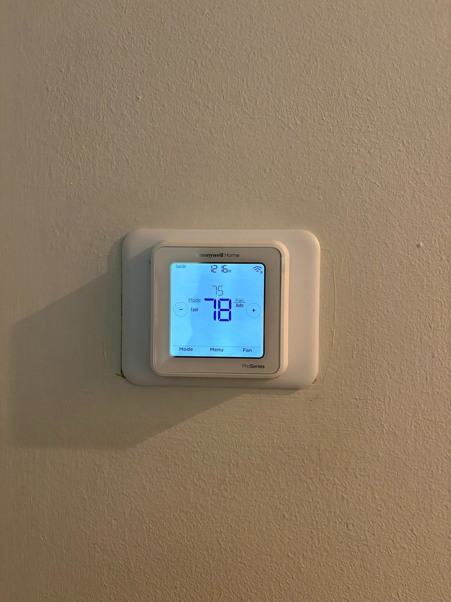 Wall-mounted digital thermostat with a blue backlit display showing 18° on a beige wall.