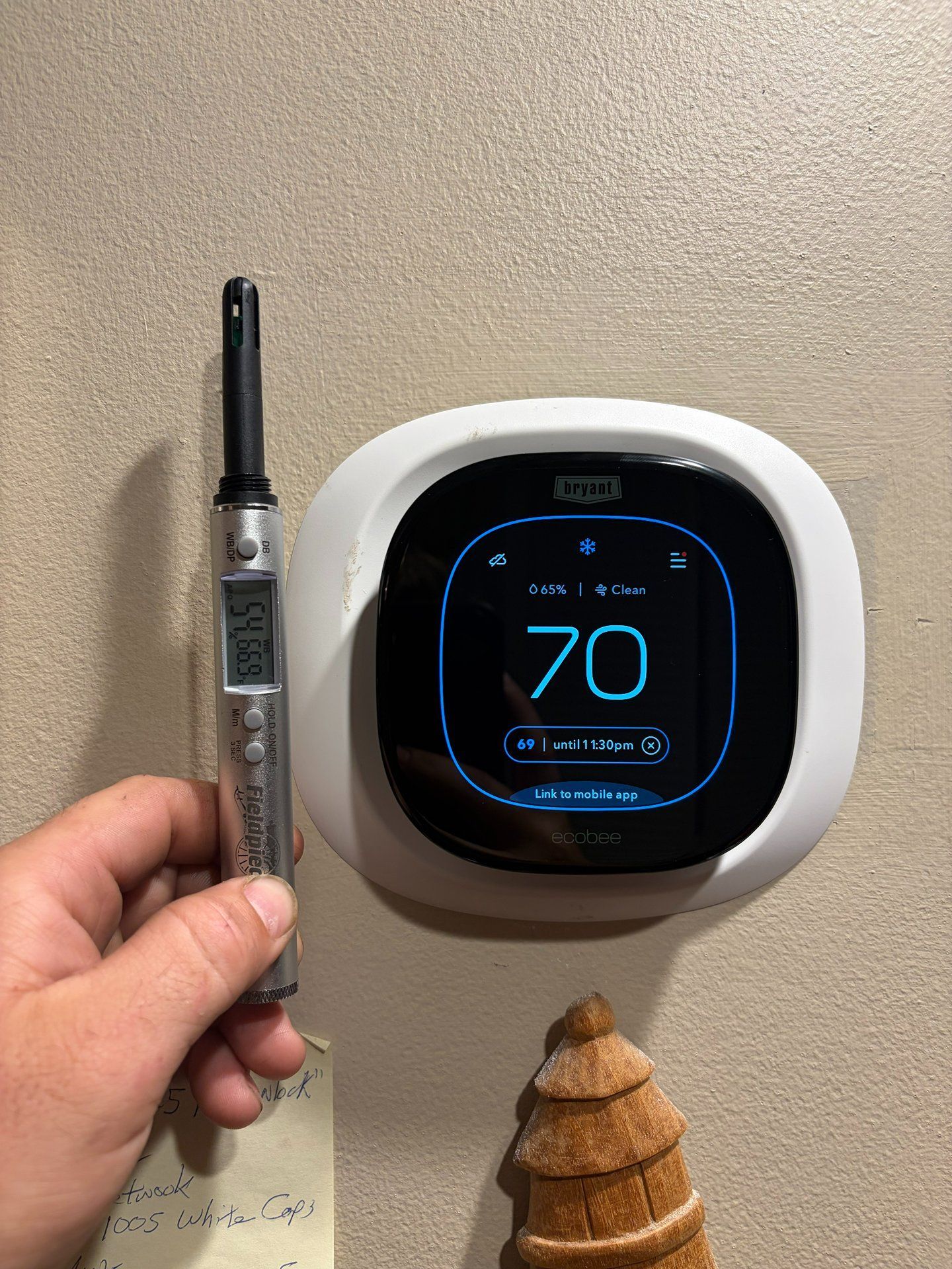 Hand holding a vape pen beside a wall-mounted Nest thermostat displaying 70°F.