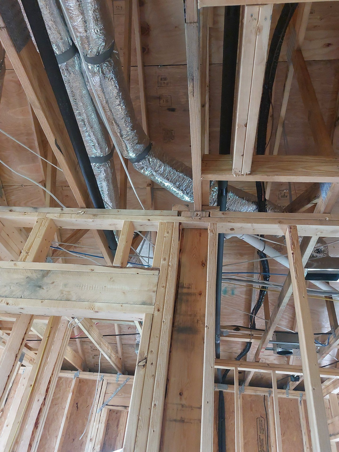 Exposed wooden framing and ductwork in an unfinished construction attic and ceiling space