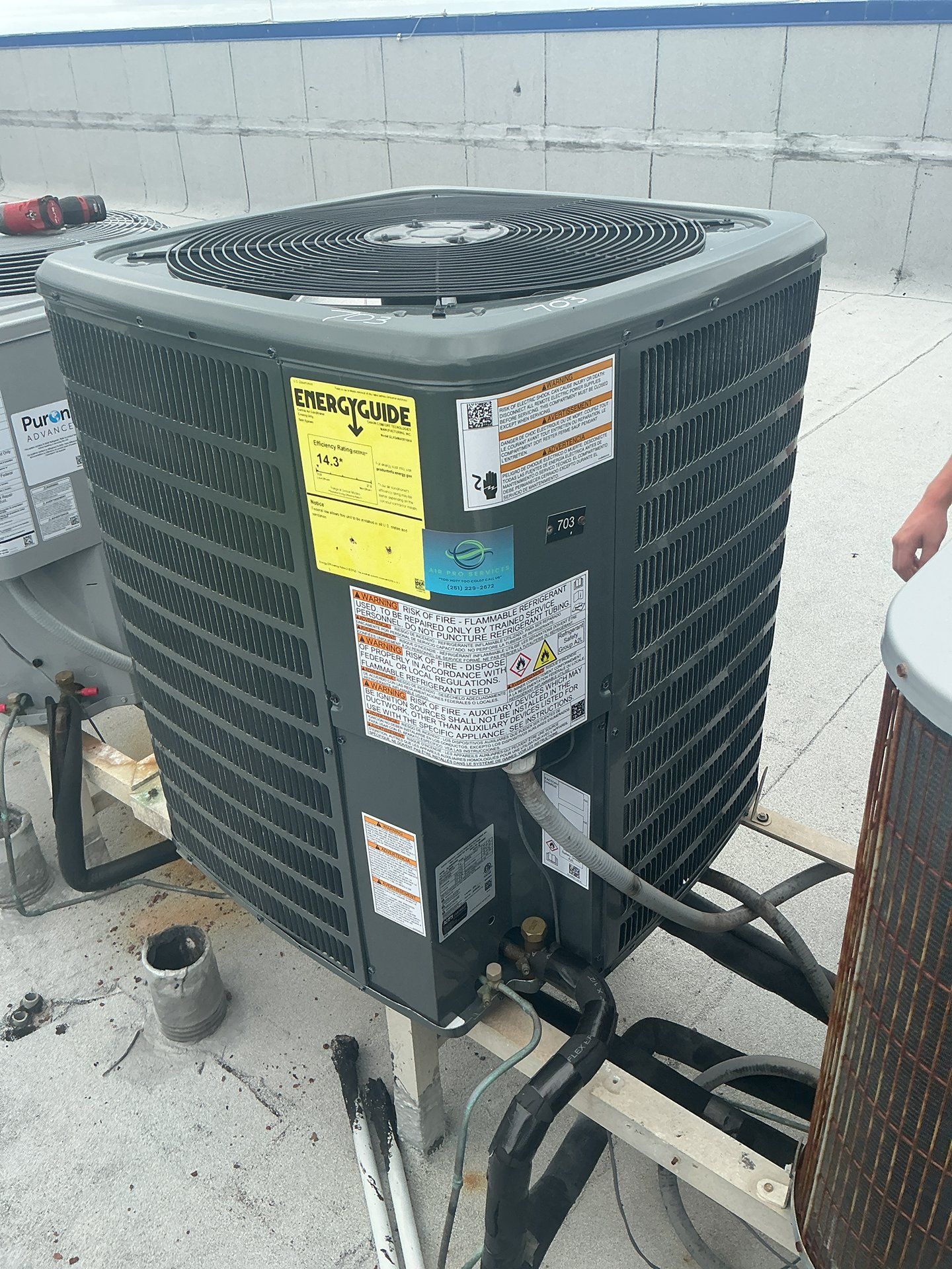Outdoor air conditioner condenser unit with black fan grille and service labels on a rooftop.