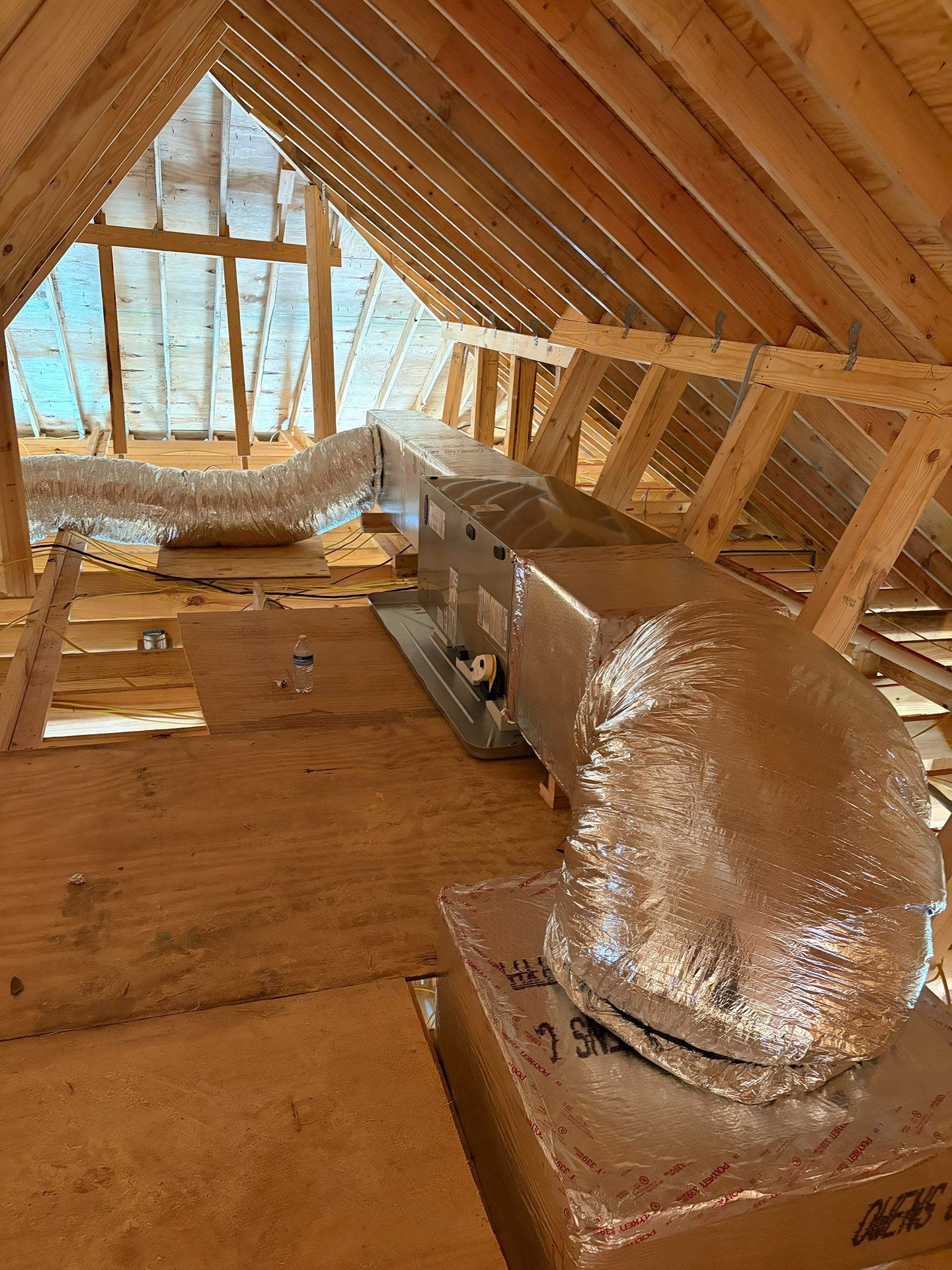 Attic under construction with exposed wooden rafters and insulated HVAC ducting.