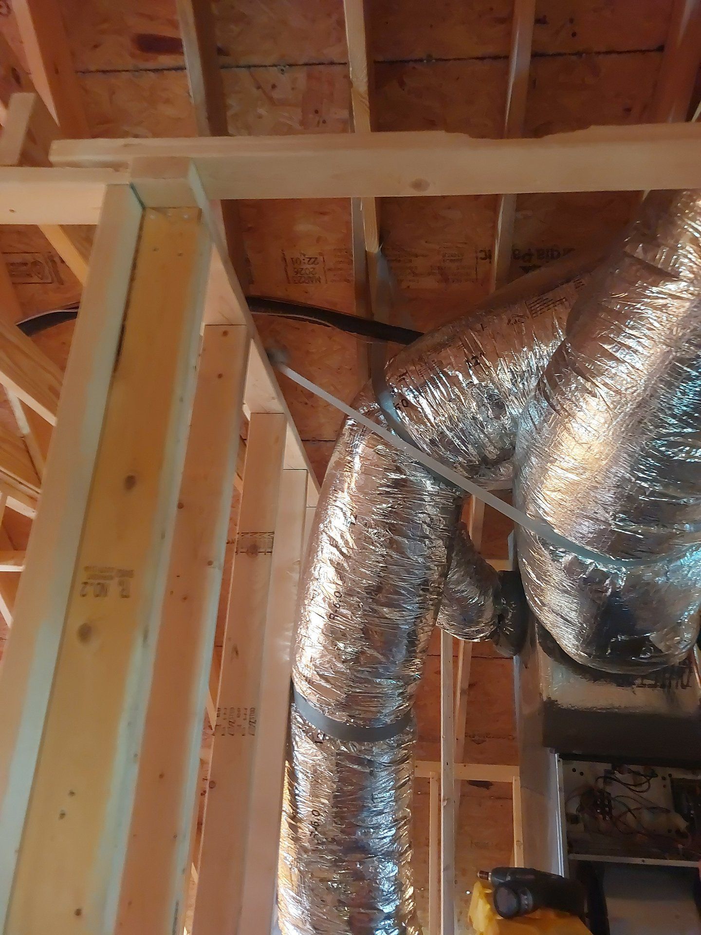 Foil-wrapped HVAC ducts in an unfinished attic with exposed wooden framing
