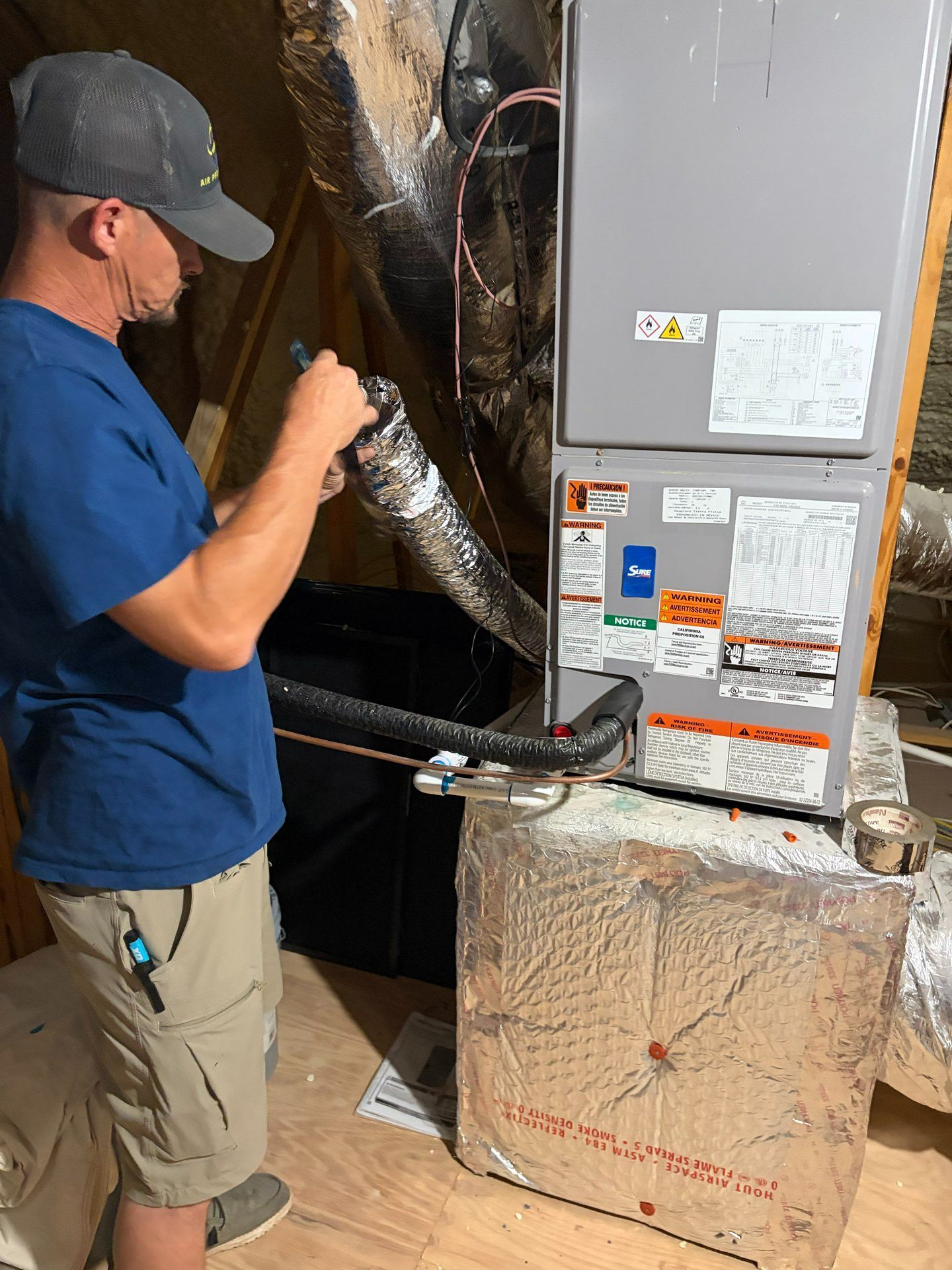 Technician inspecting HVAC ductwork beside a metal furnace in a utility room