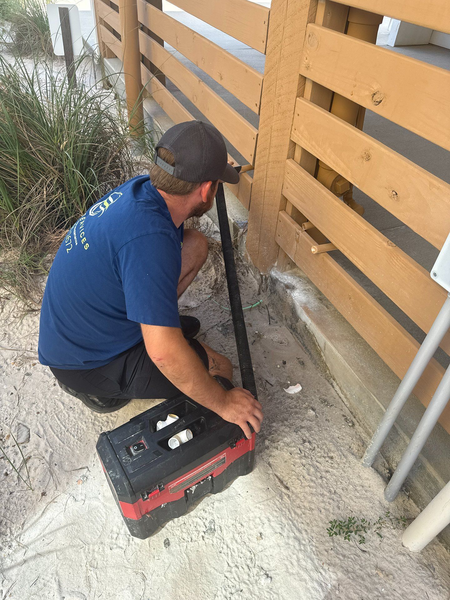 Technician kneels beside a wooden fence, inspecting or repairing a post with tools on the ground.