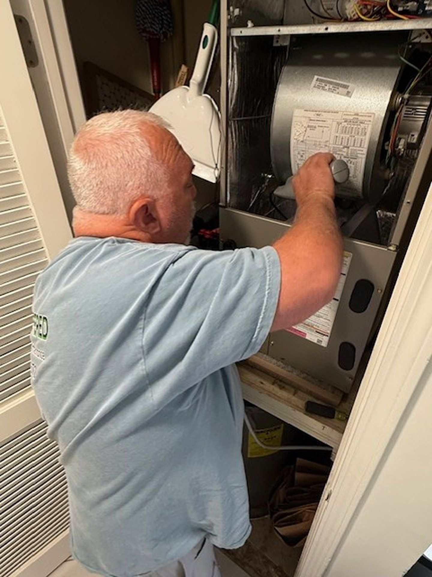 Person inspecting the inside of an HVAC unit in a closet, reaching toward the fan assembly.