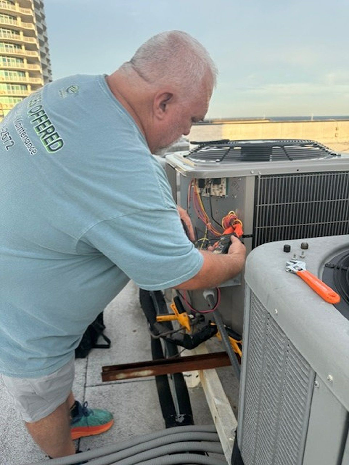 Technician in light blue shirt repairing rooftop HVAC unit at sunset