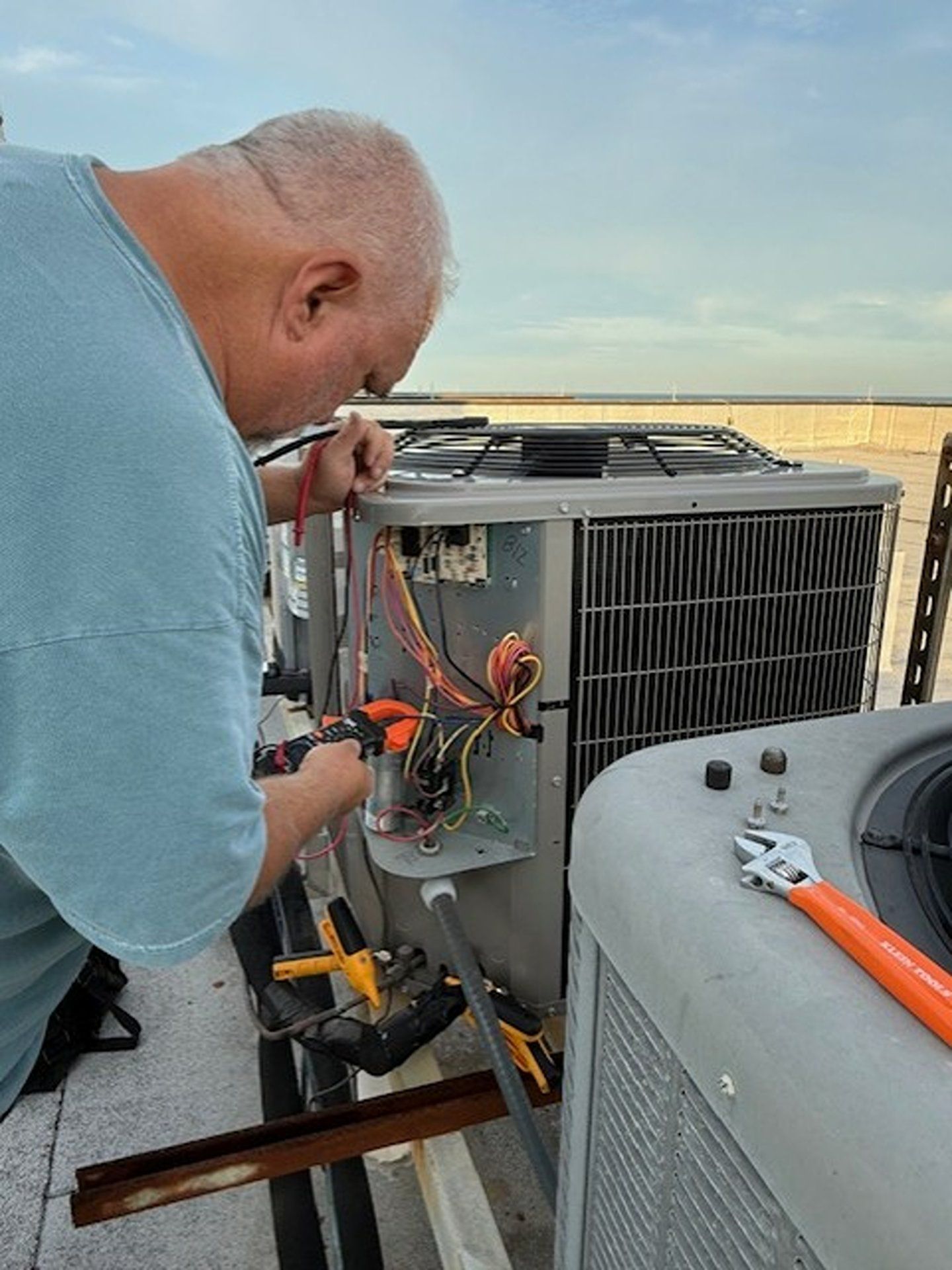 Technician repairs rooftop HVAC unit, using tools with orange cables and gray equipment nearby.
