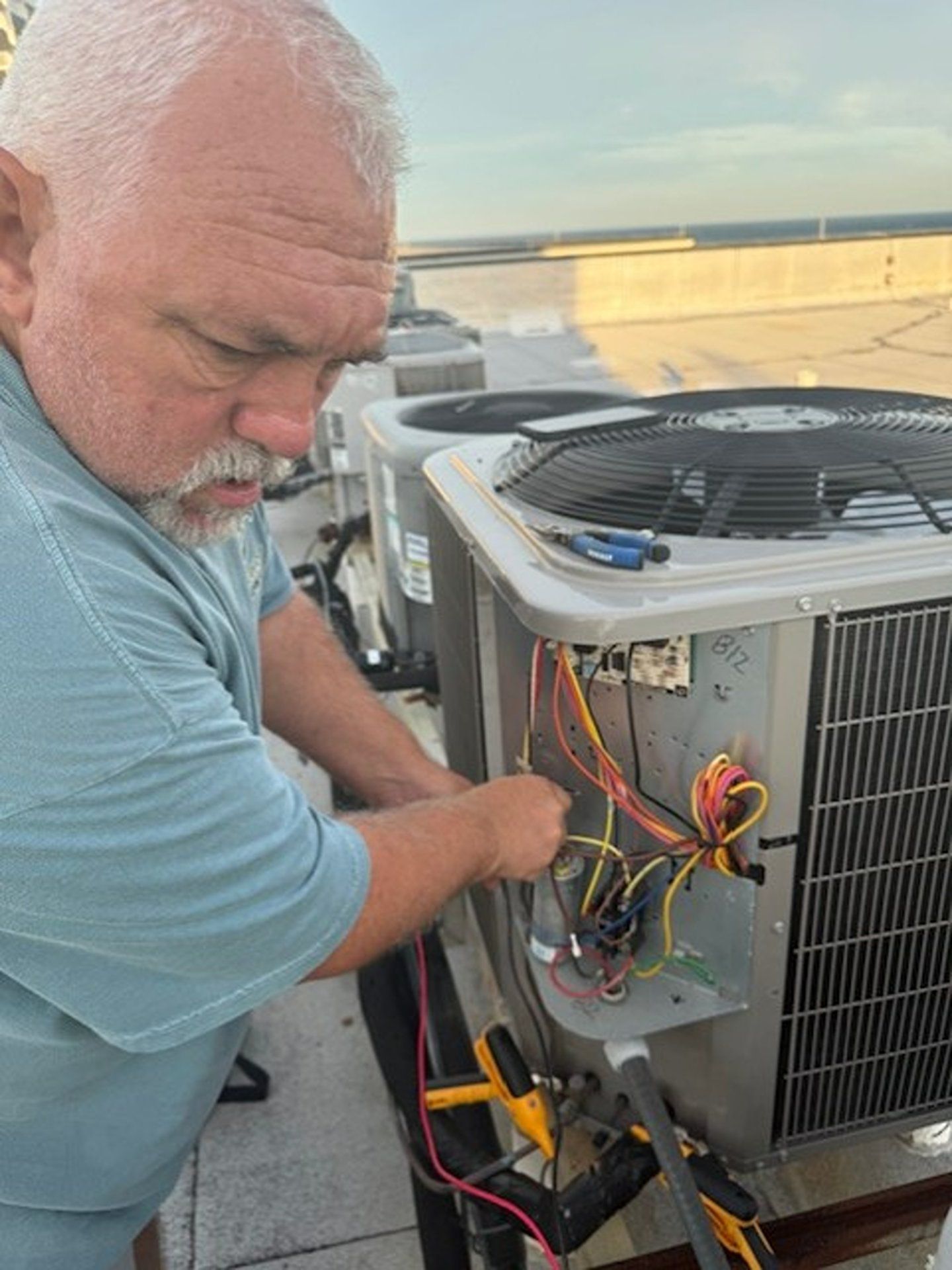 Technician repairs rooftop HVAC unit, exposing wiring and components.