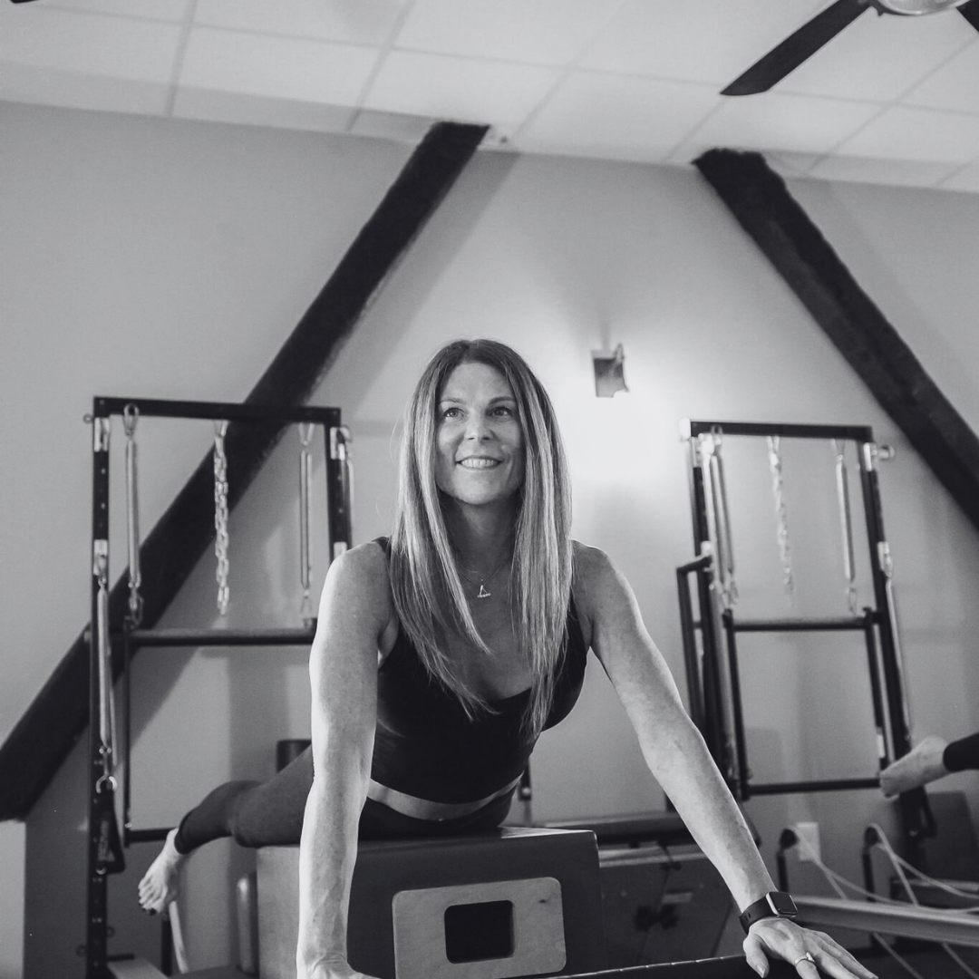 A woman is sitting on a pilates machine and smiling