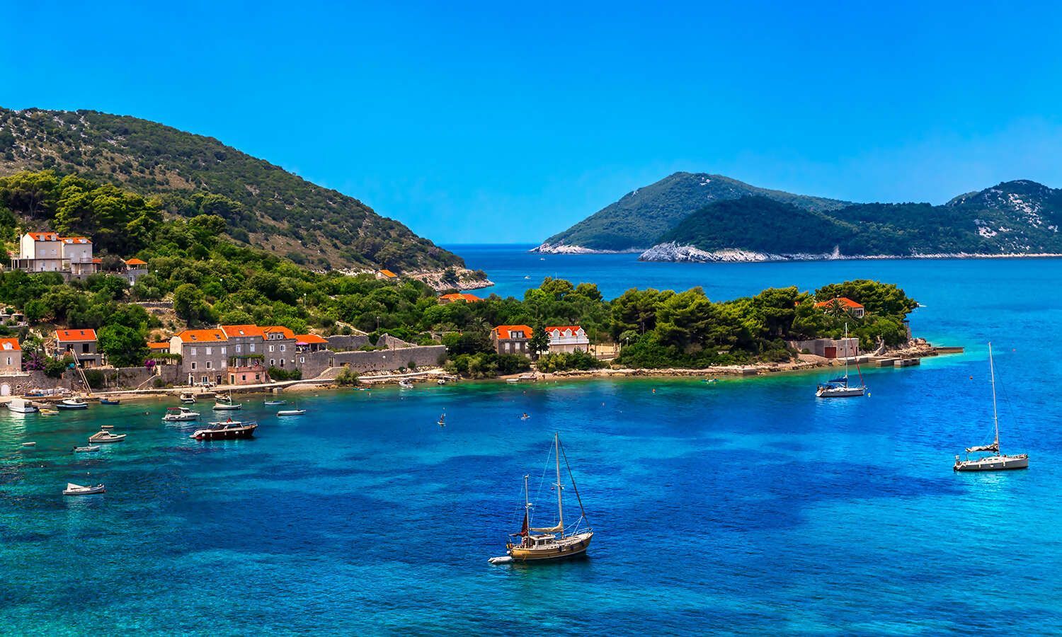 A small island in the middle of the ocean with boats in the water.
