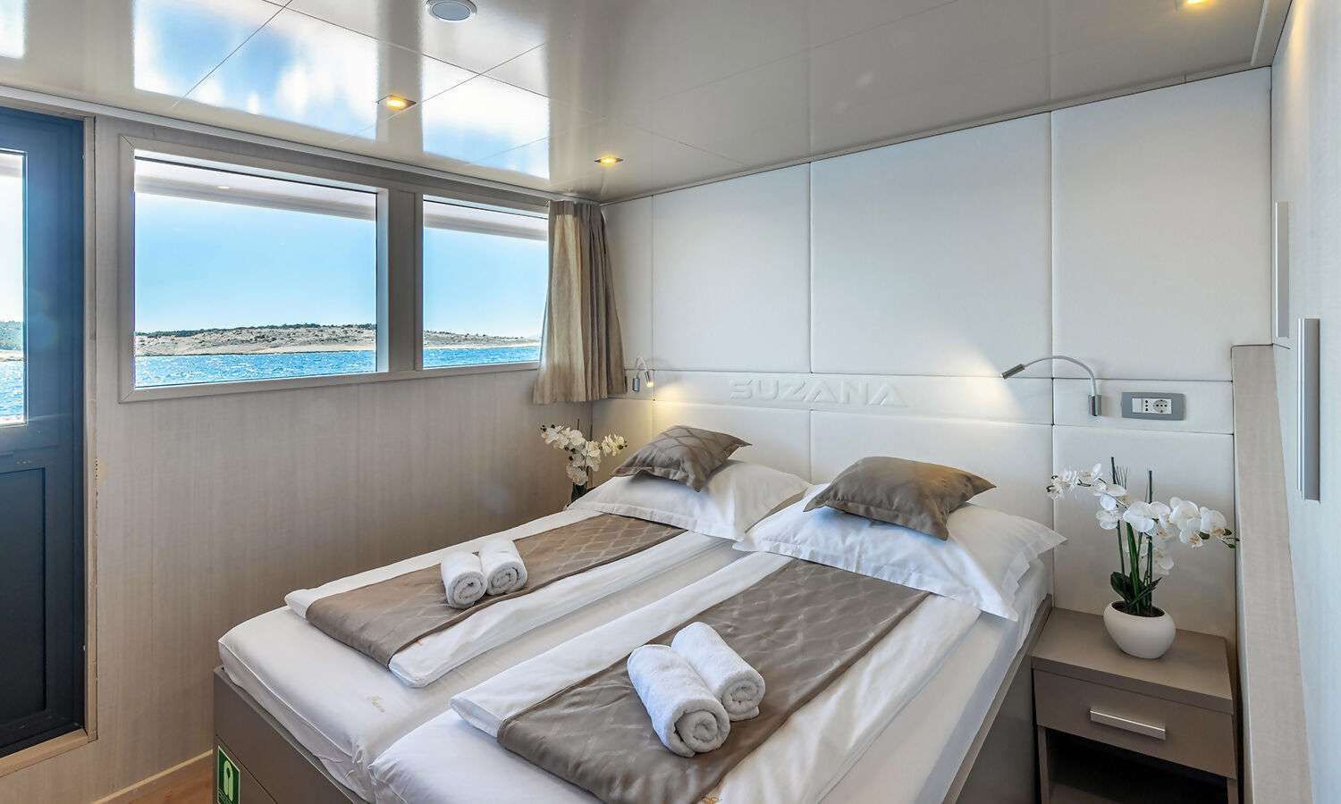 A bedroom on a boat with two beds and a nightstand.
