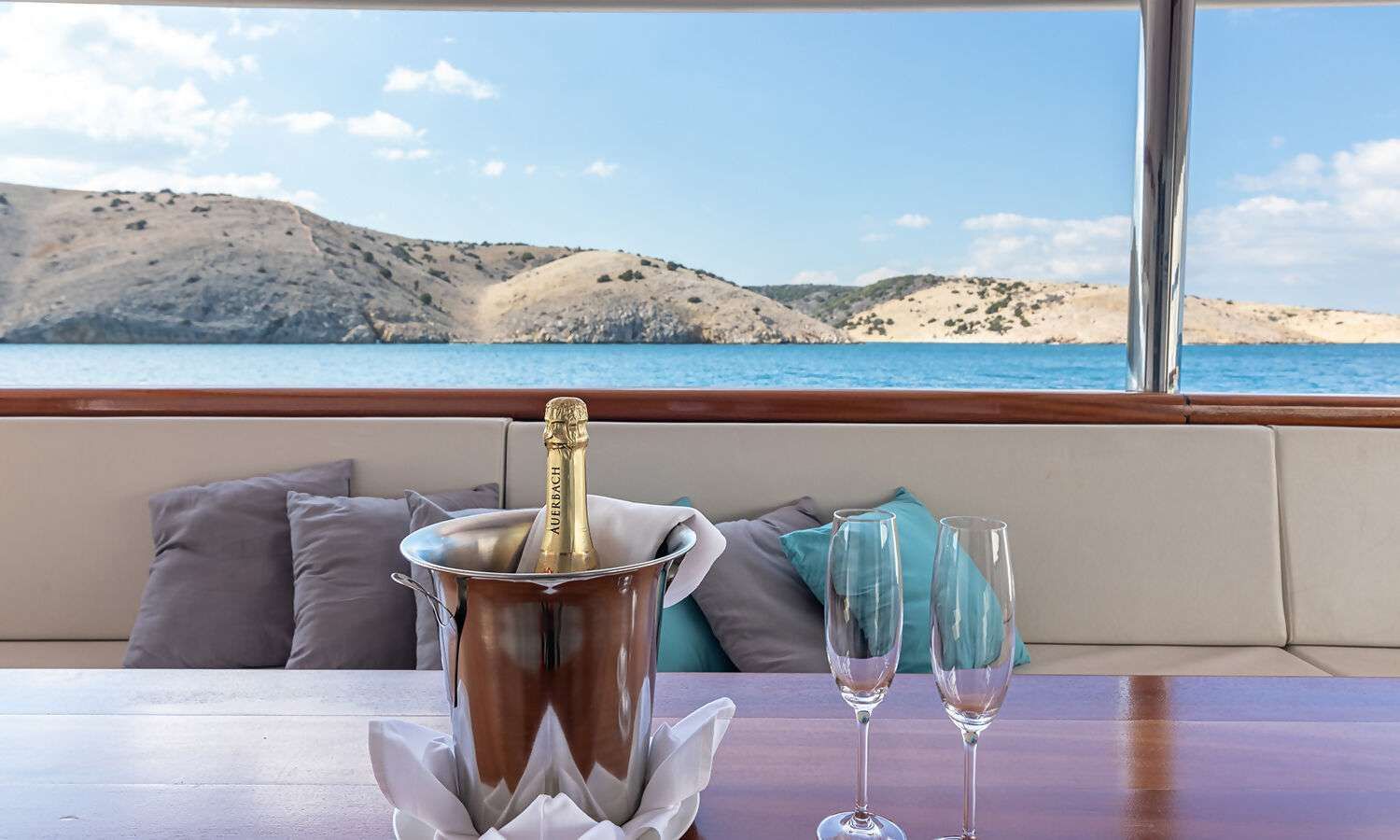 A bucket of champagne and two glasses on a table with a view of the ocean.