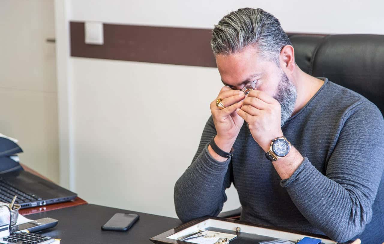 Ein Mann sitzt an einem Schreibtisch und reibt sich nachdenklich die Augen, die Hände in der Nähe seines Gesichts gefaltet.