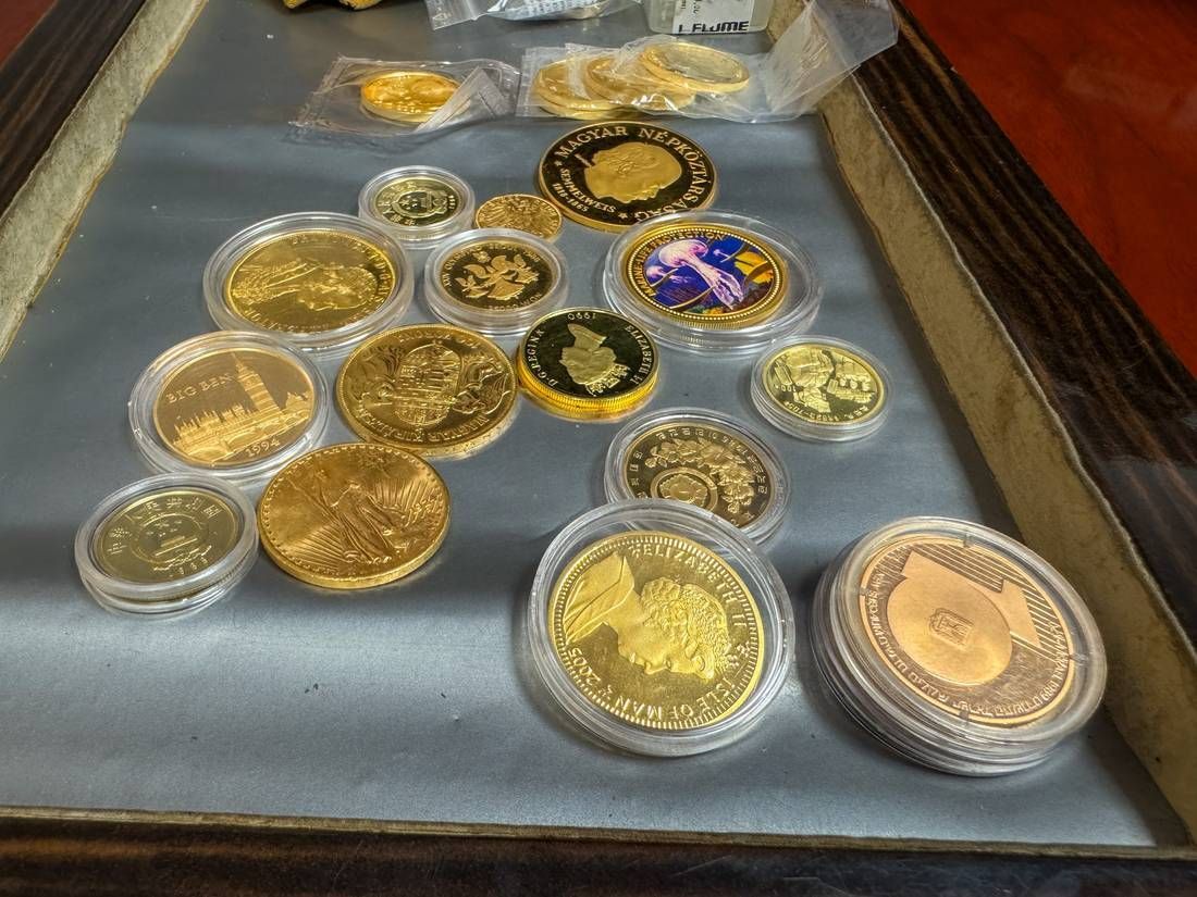 Verschiedene goldene und bunte Gedenkmünzen in durchsichtigen Etuis auf einem blauen Tablett.