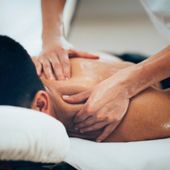 A person receives a back massage, with a therapist's hands kneading the skin near their shoulder and upper back.