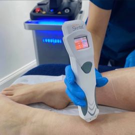 A technician in blue gloves uses a handheld laser device on a patient's leg during a clinical treatment.