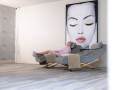 A person in a light pink robe reclines in a gray chair, relaxing in a room decorated with Christmas trees and wall sconces.