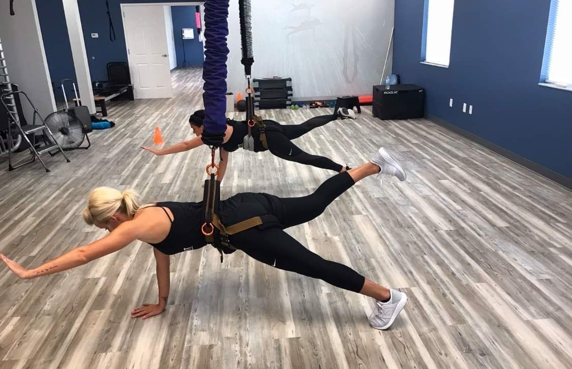 Two women are doing aerial yoga in a gym.