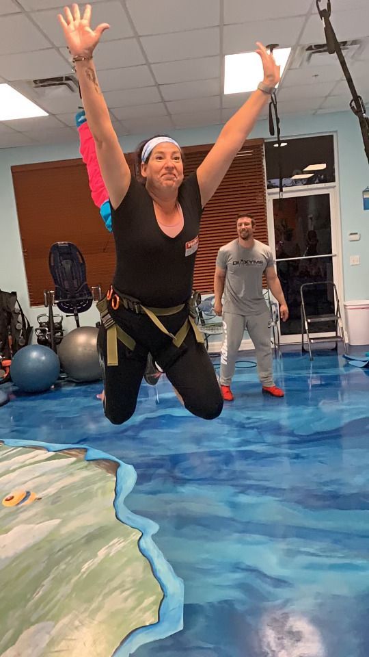 A woman is jumping in the air in a gym while a man watches.