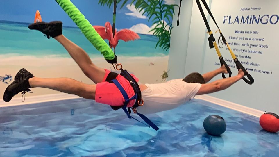 A man is doing exercises in a pool with flamingos on the wall.