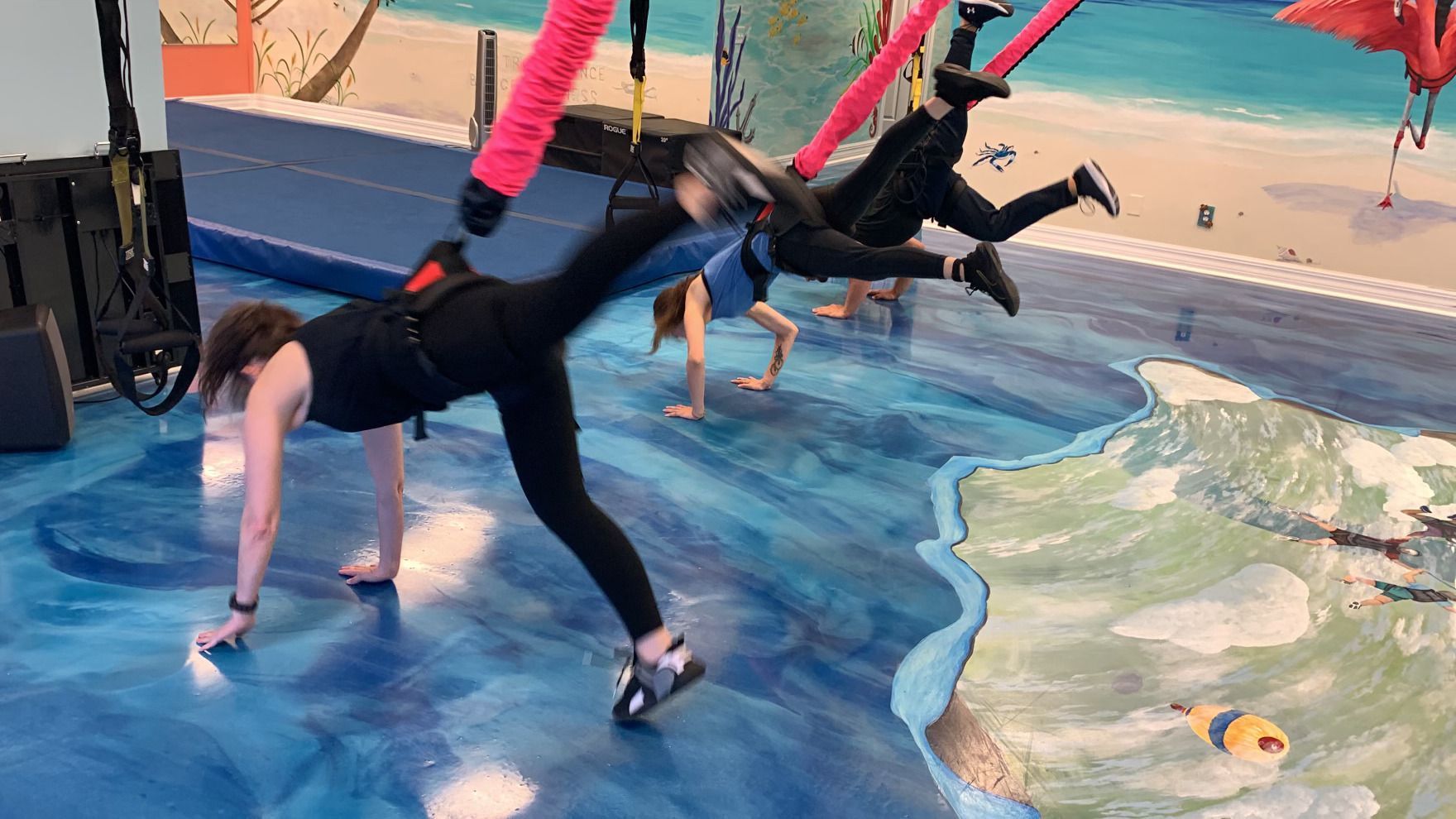 A group of people are doing aerial yoga in a gym.
