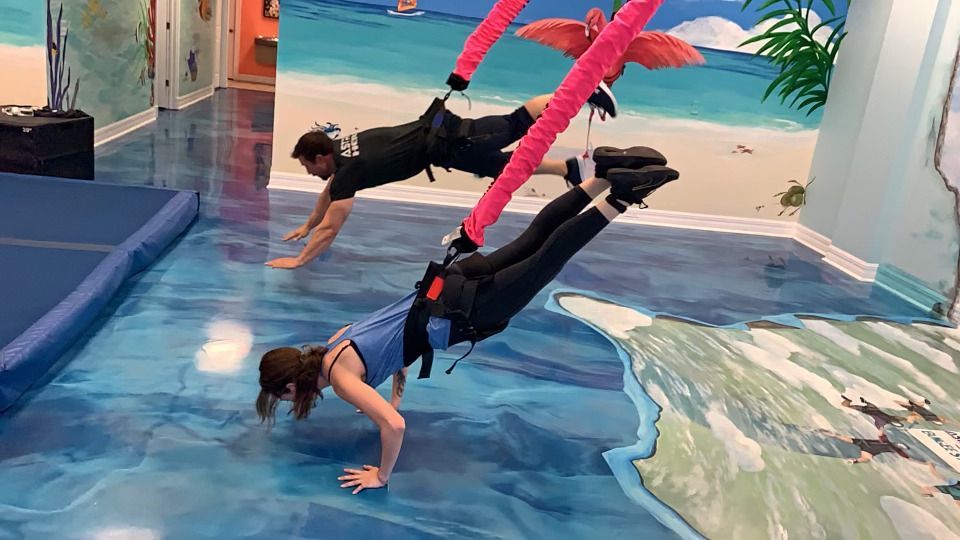 A man and a woman are doing push ups on a bungee cord in a gym.