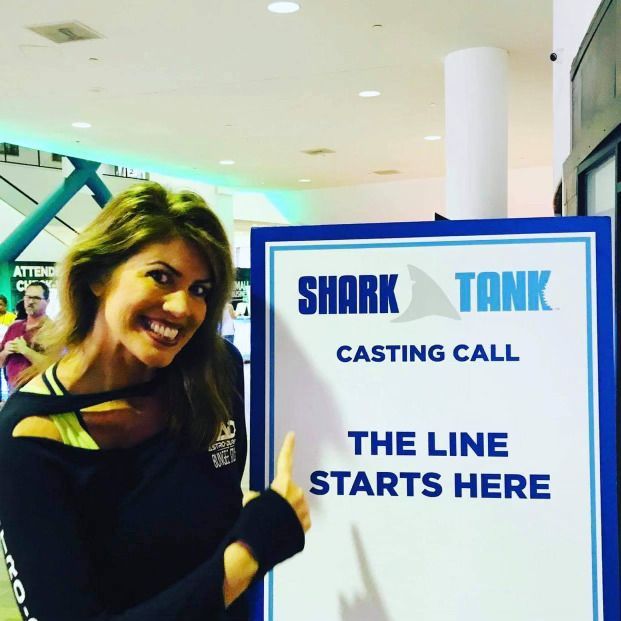 A woman holding a sign that says shark tank casting call the line starts here
