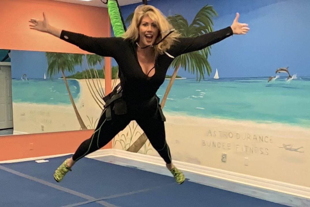 A woman is jumping in the air in a gym with her arms outstretched.