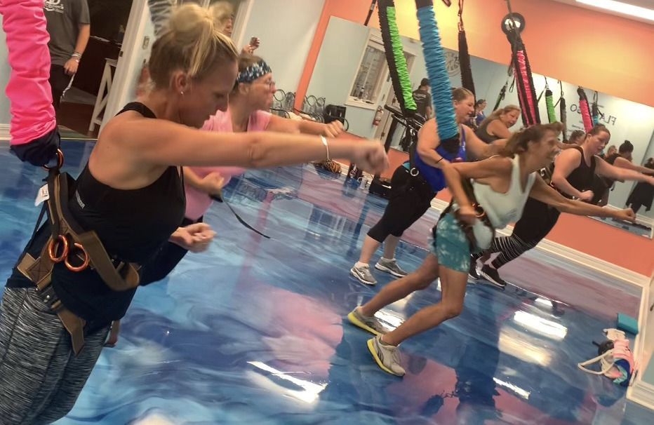 A group of people are doing aerial yoga in a gym.