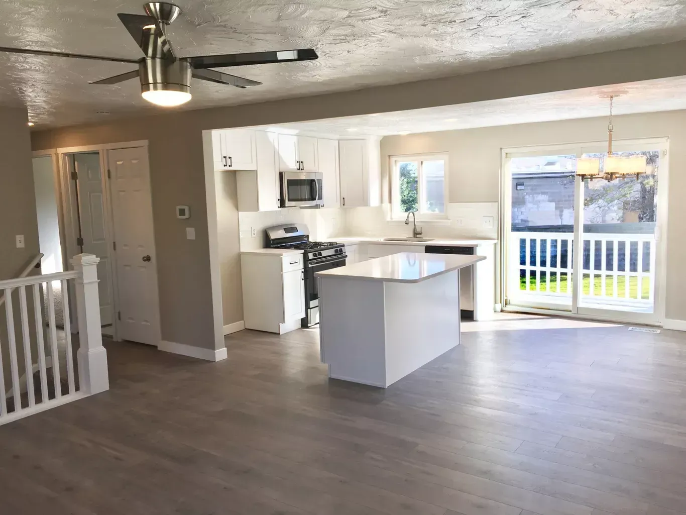 Open-concept kitchen and living room with white cabinets, island, sliding glass door, and gray flooring.