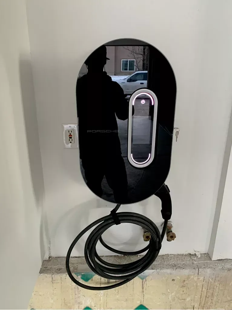 Electric vehicle charger mounted on a wall; black and silver design with a coiled cable.