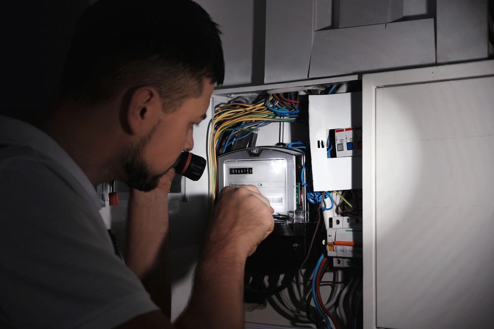 Man using a flashlight to inspect an electrical panel. Dark setting.