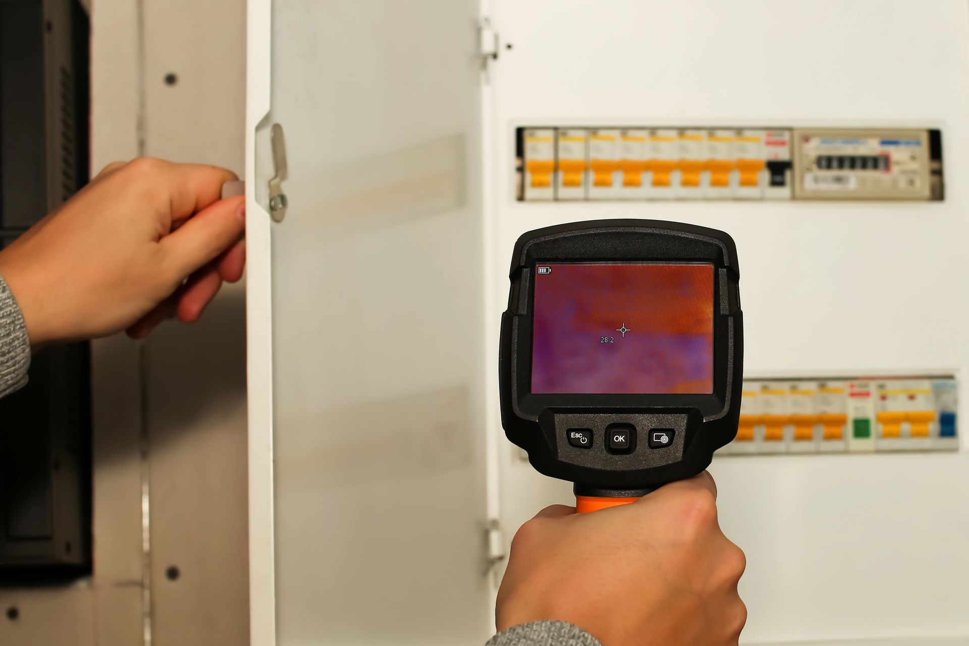 Person using a thermal camera on an electrical panel to check for overheating; indoor setting. Person using a thermal camera on an electrical panel to check for overheating; indoor setting.