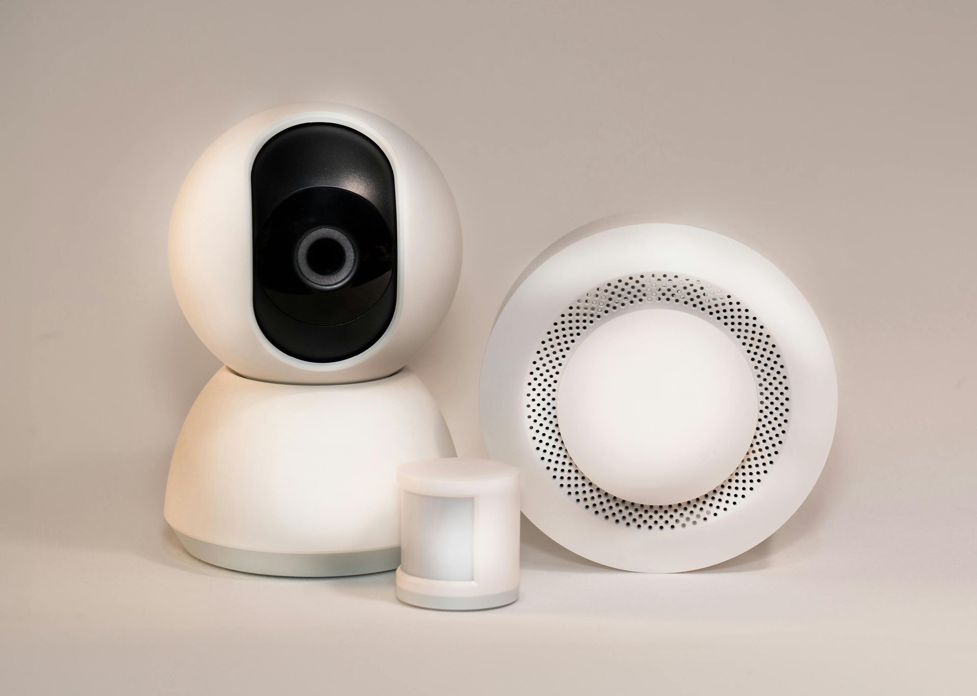 White security camera, motion sensor, and speaker on a light background.