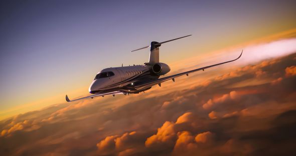 Jet airplane flying above orange and gold clouds at sunset.