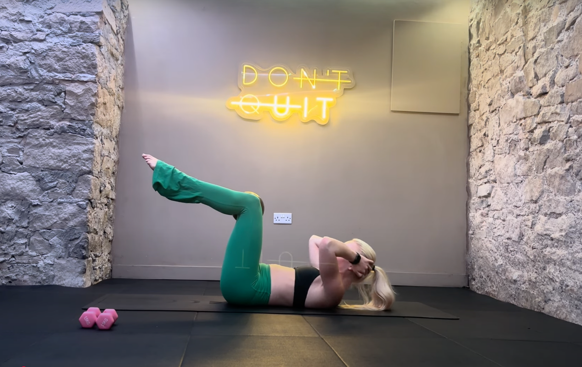 Woman in yoga pose, smiling, wearing black bra and light green pants, sitting on a mat. 