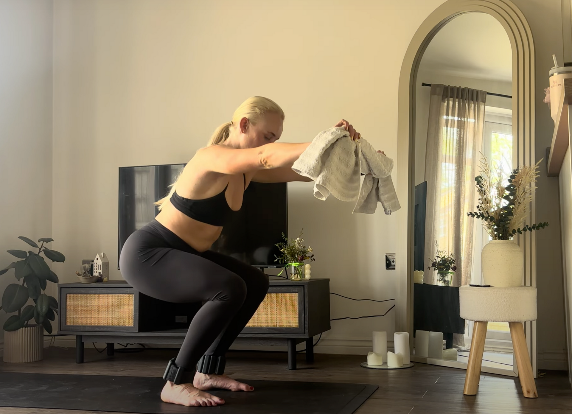A woman in workout clothes performs a bird dog exercise on a mat in a gym. The neon sign behind her reads 