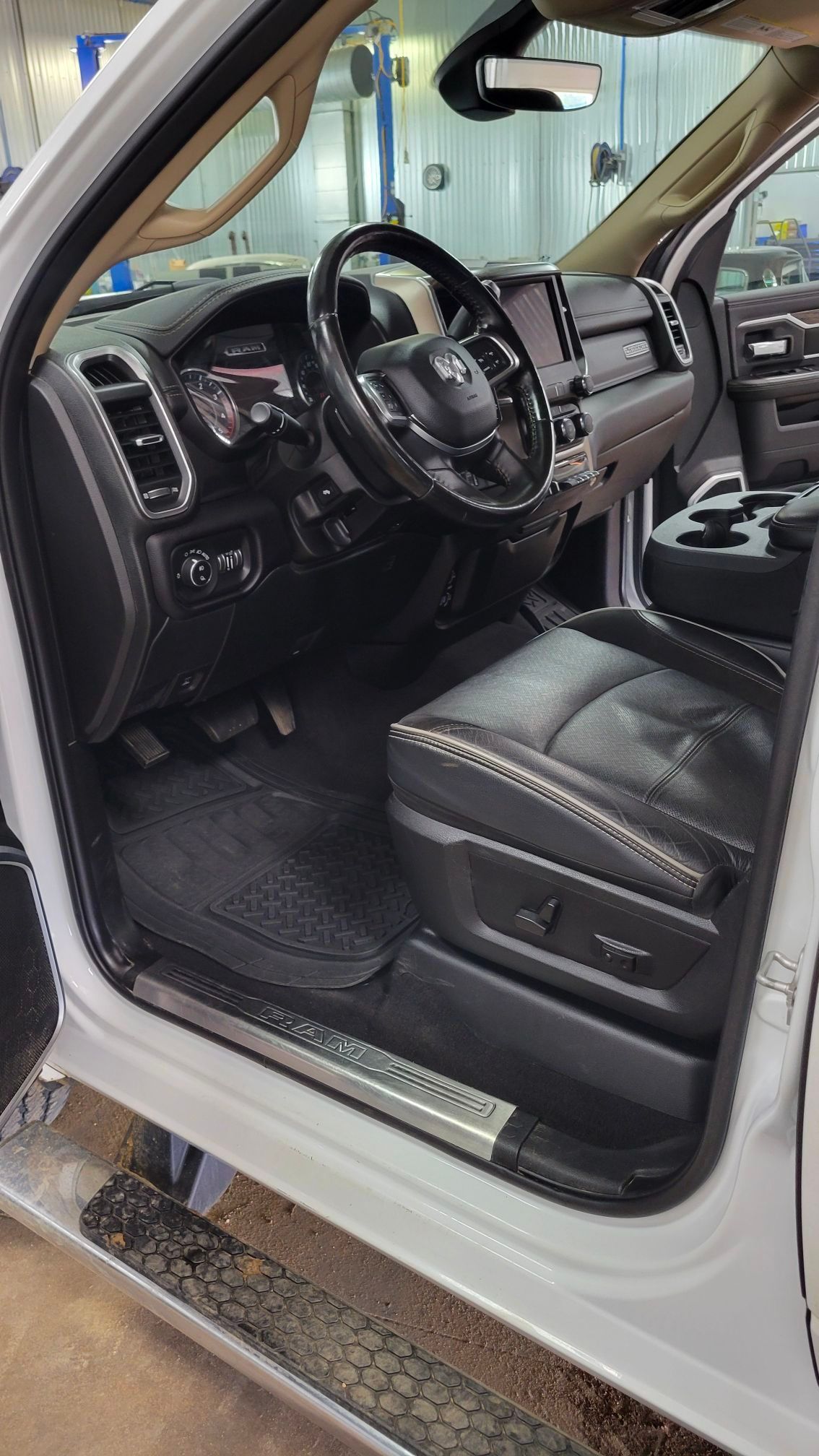 Interior view of a white truck, black leather seats, steering wheel, dashboard, and floor mats.