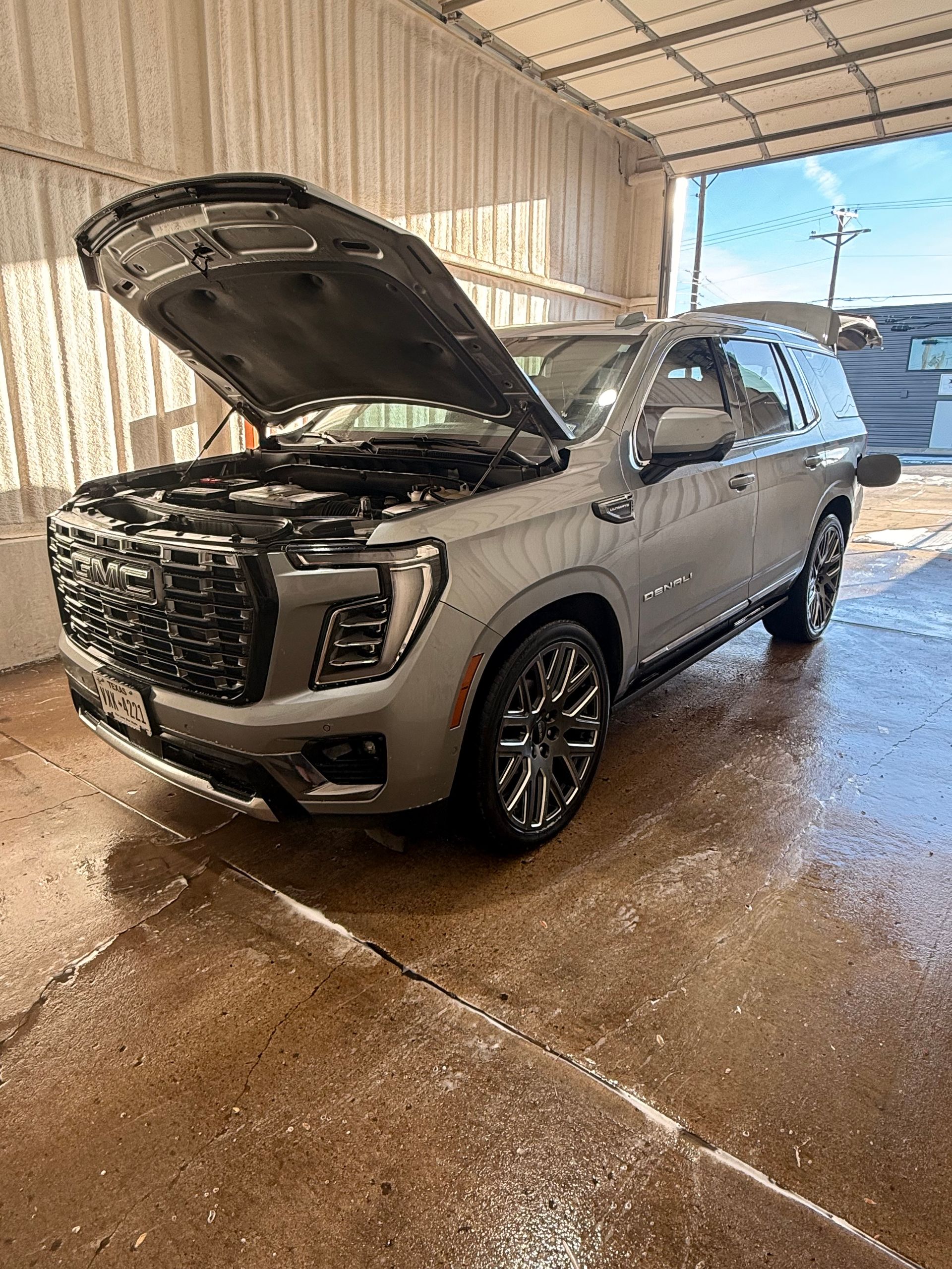A silver SUV with its hood open, parked in a wet indoor car wash bay.