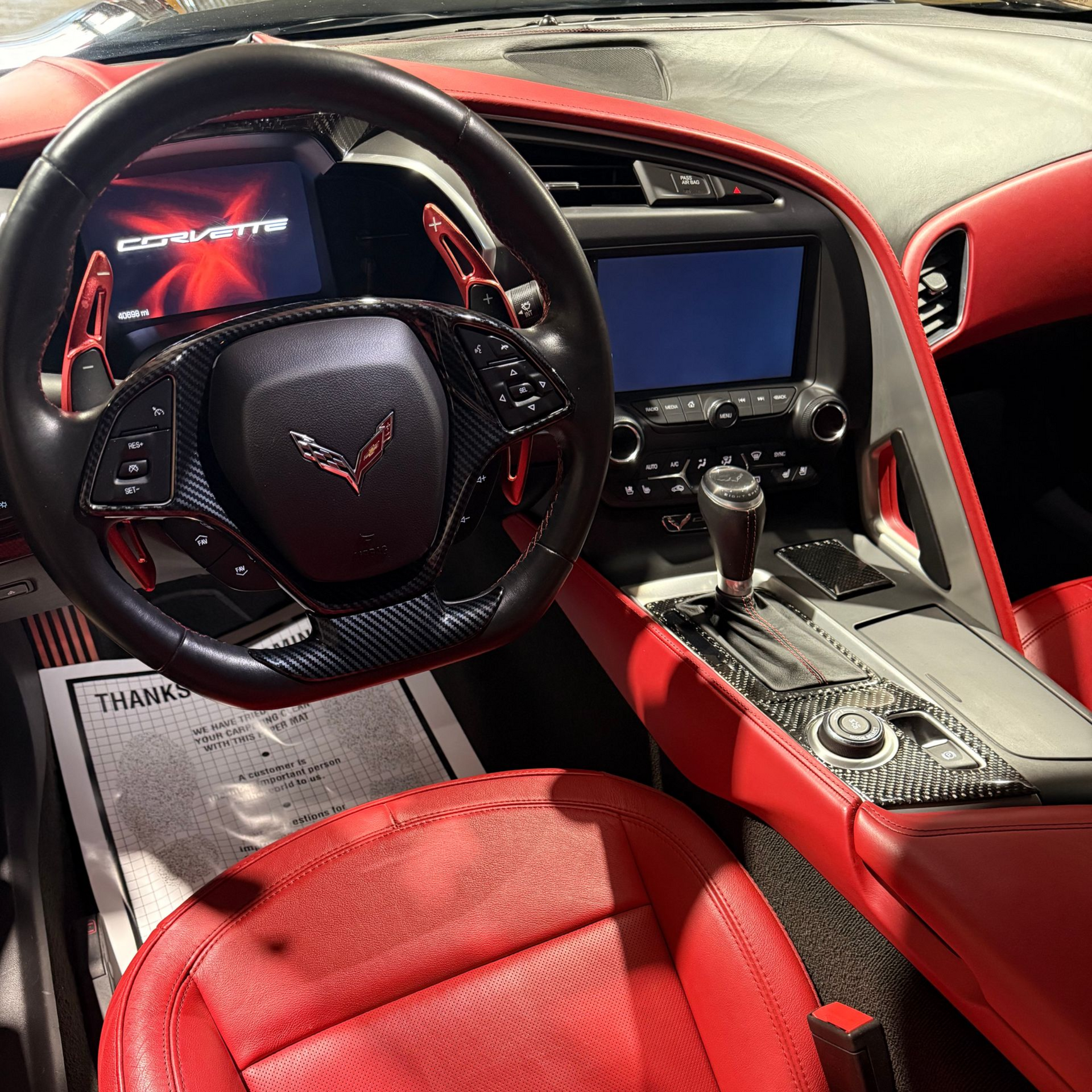 Interior of a Chevrolet Corvette featuring a black steering wheel, red leather seats, and a carbon fiber center console.