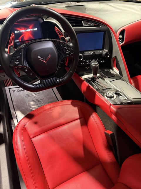 Interior of a Chevrolet Corvette featuring a black steering wheel, red perforated leather seats, and a dashboard screen.
