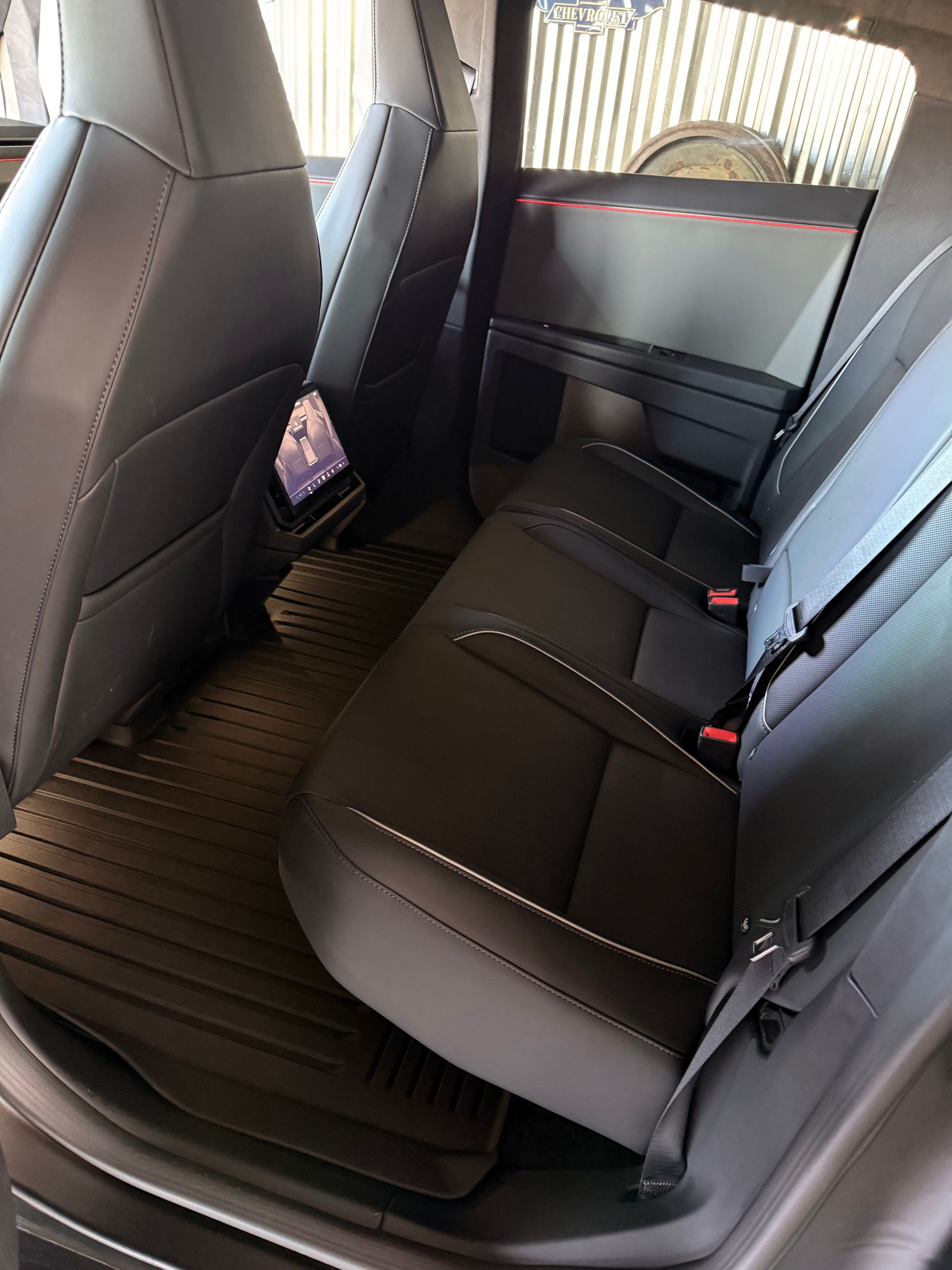 The back seat of a modern vehicle with dark gray leather upholstery, textured floor mats, and a small center screen.