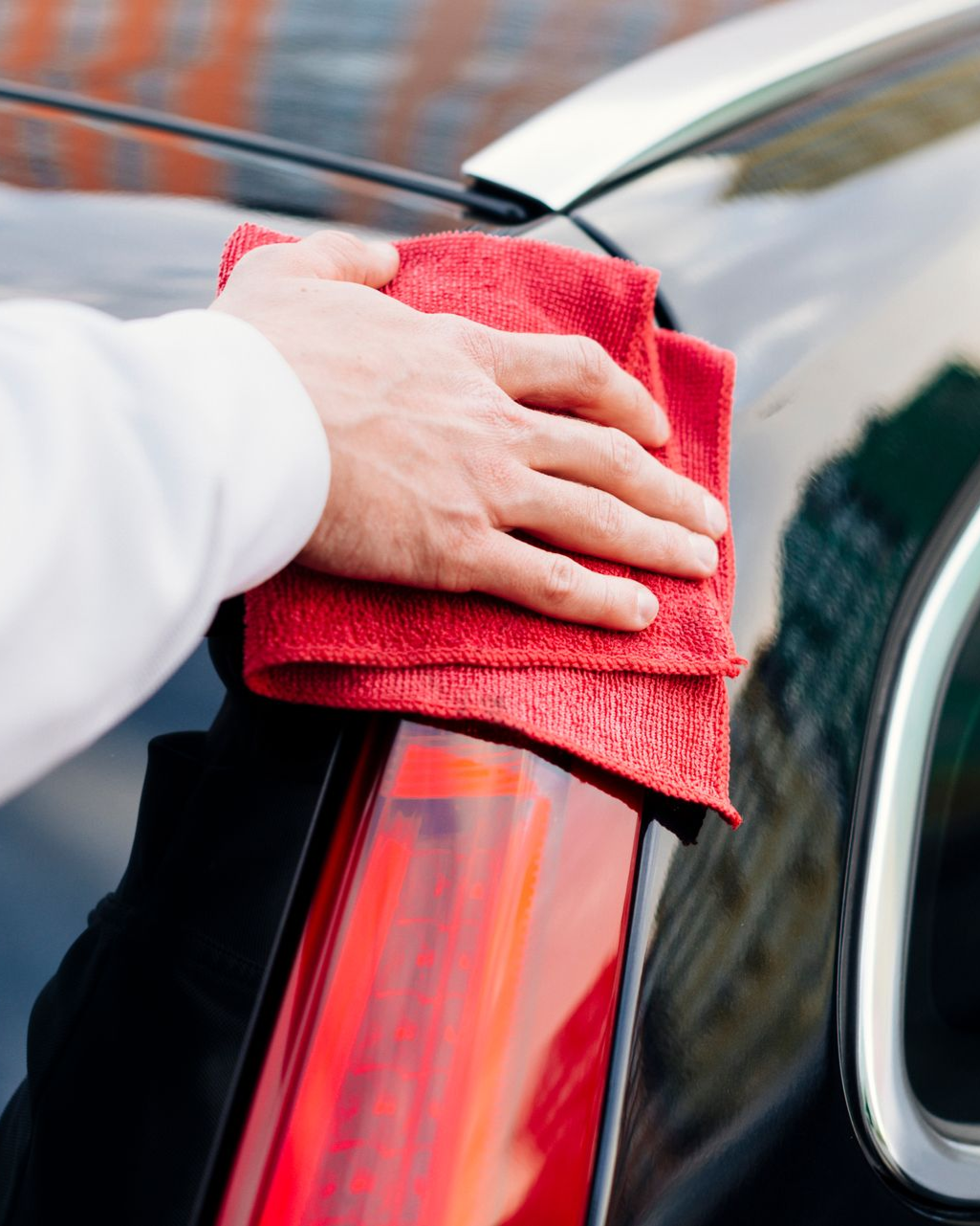 A hand using a red microfiber cloth to polish the rear taillight and body of a black car.