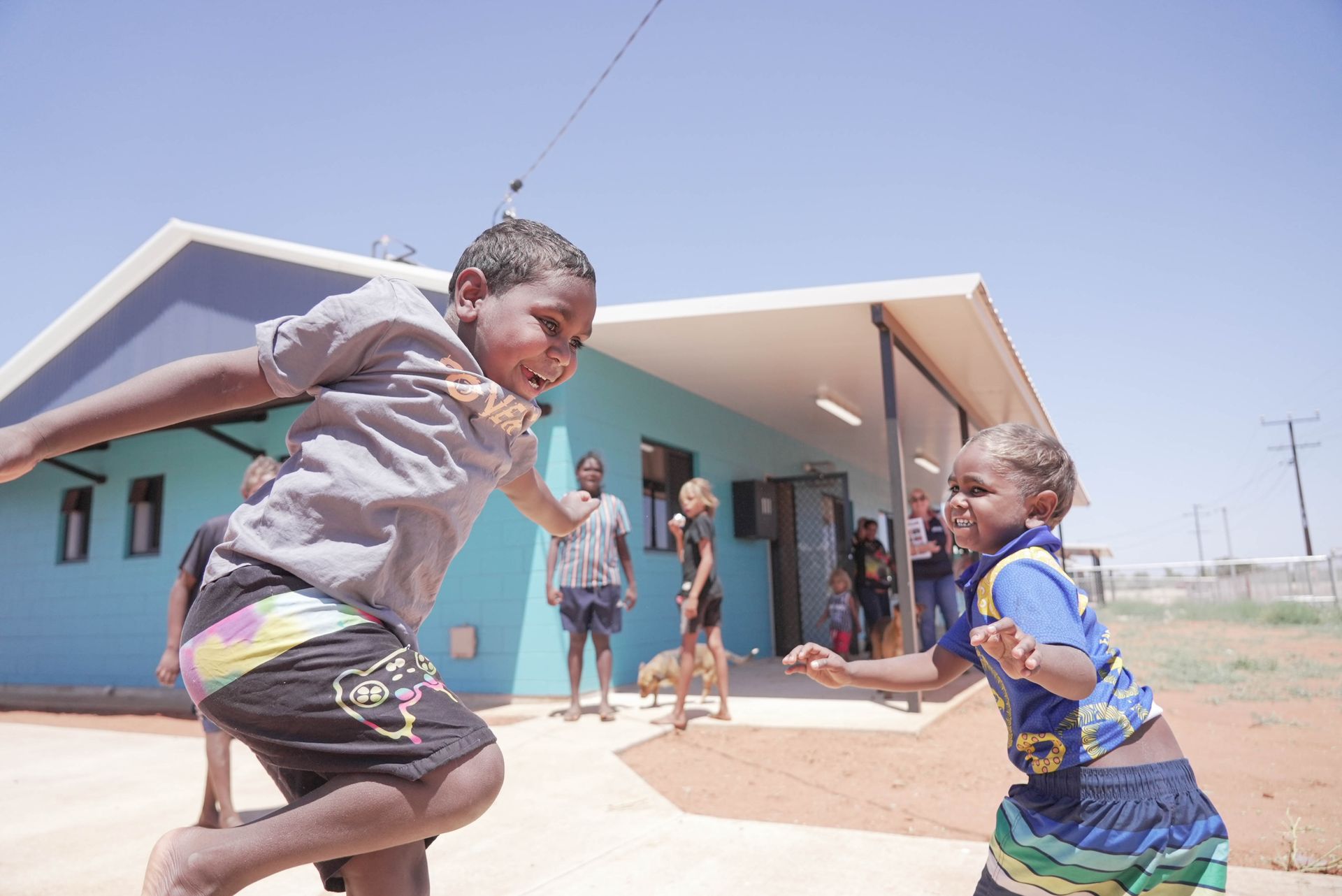 Children playing joyfully outside a blue building in the sun.
