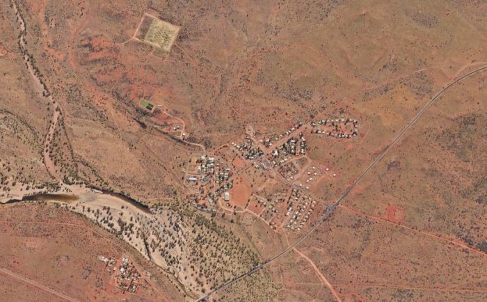 Aerial view of a small settlement in an arid, red-earth landscape, with a river running nearby.