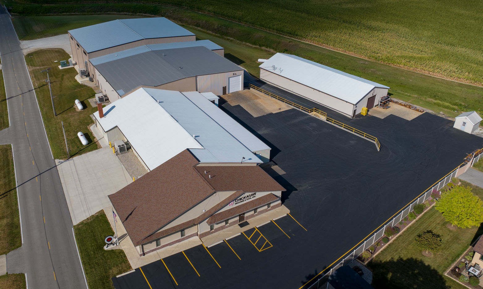Aerial view of a business with a brown roof and a large, black parking lot in a rural setting.