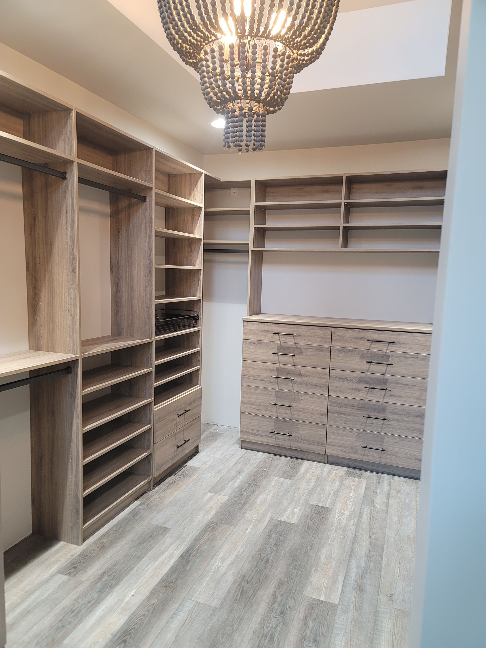 Walk-in closet with built-in wood shelving, hanging rods, drawers, and a chandelier