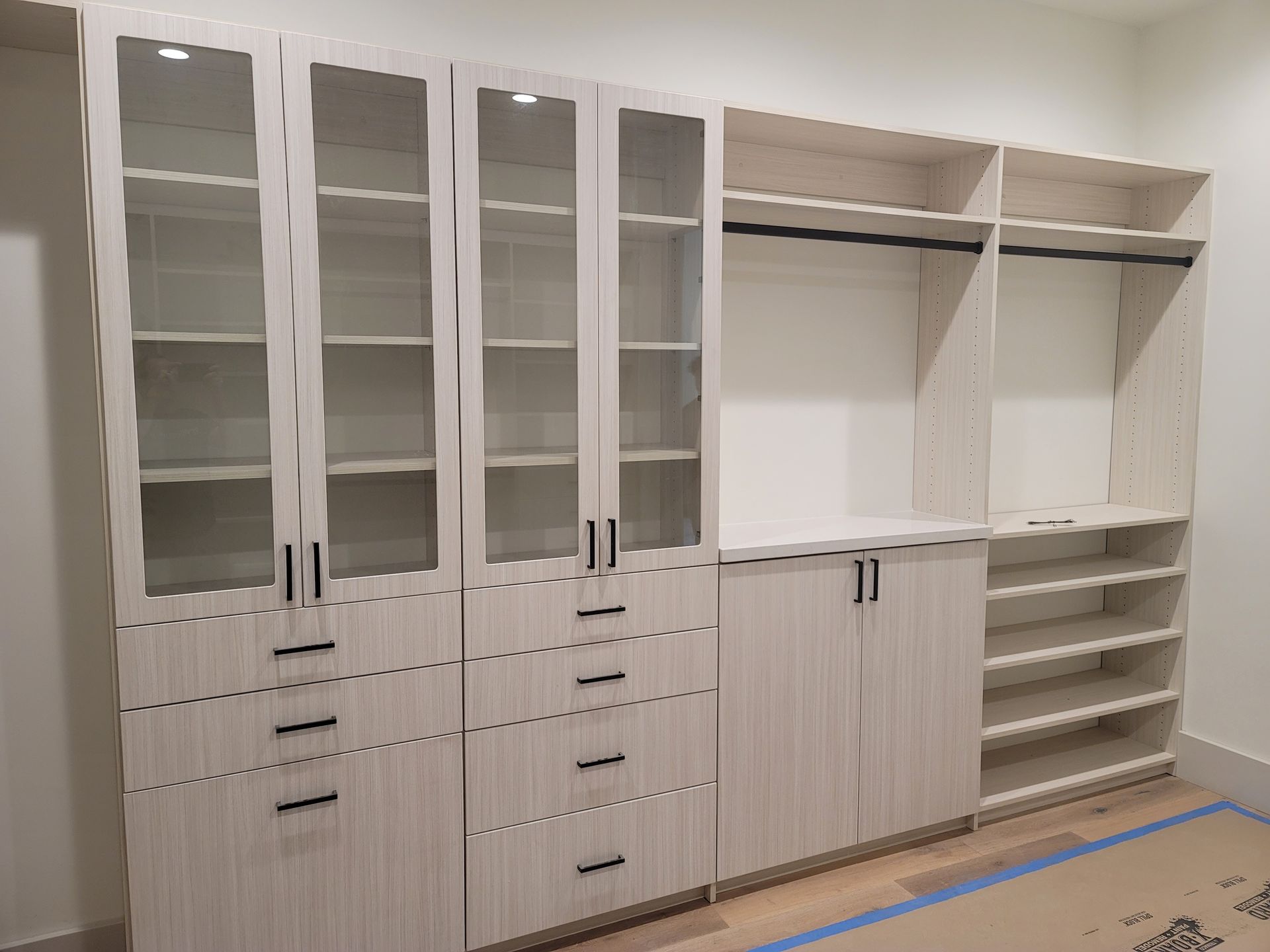 Built-in white closet cabinetry with glass doors, drawers, and open shelving in a room under renovation