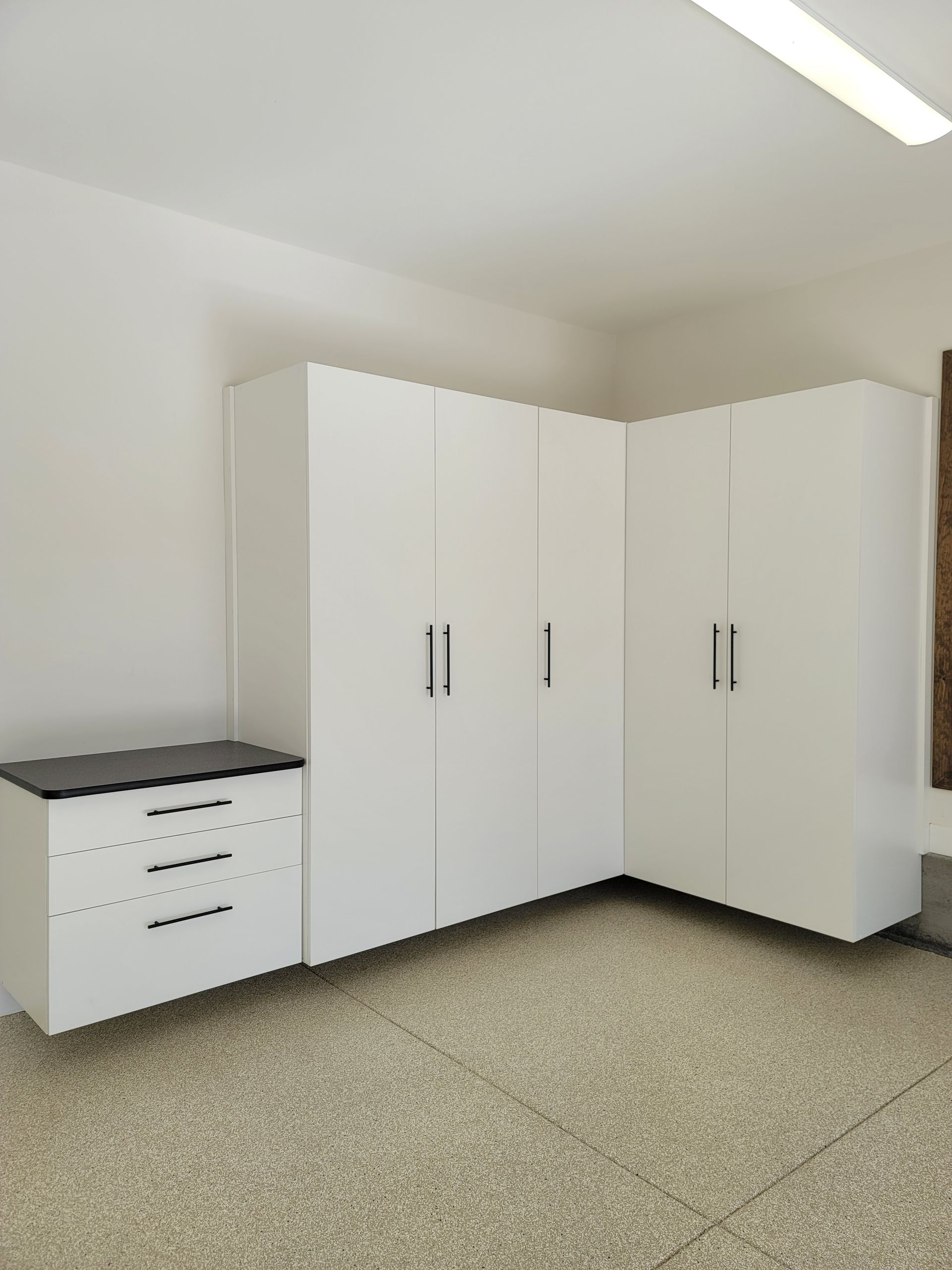 White storage cabinets and a small drawer unit in a plain room with speckled flooring.